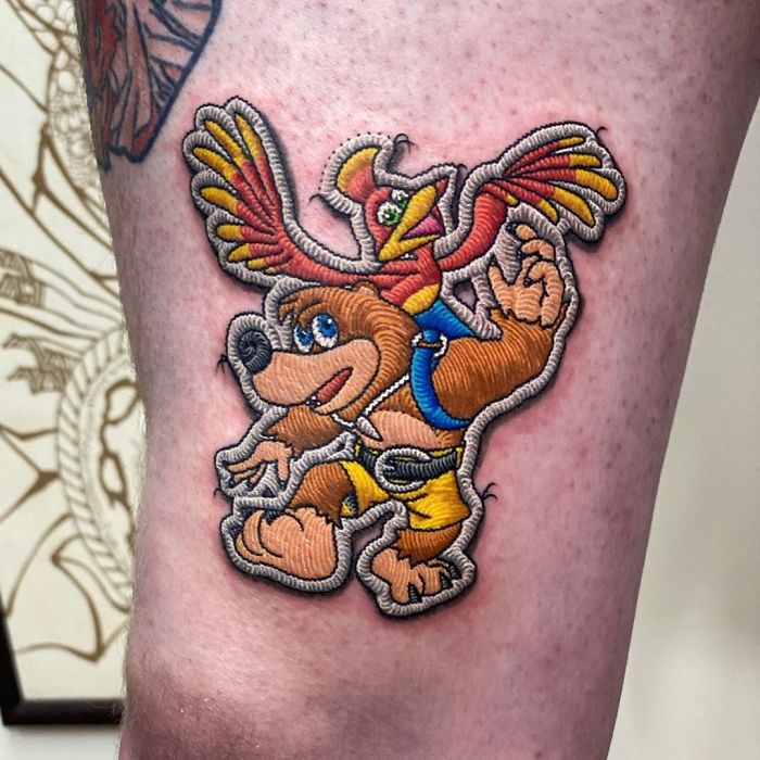 Tattoo of a bear and bird character resembling a sewn-on patch, showcasing impressive artistry.