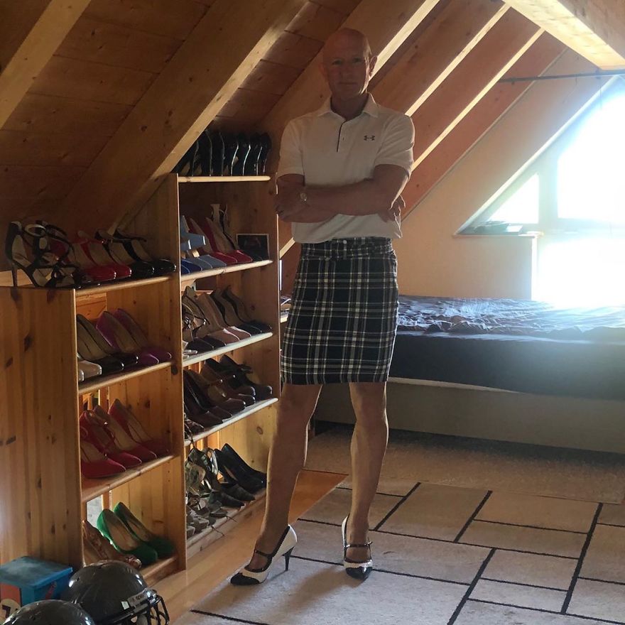Mark Bryan is wearing a white T-shirt, plaid skirt, and white black high heels and standing near high heel closet