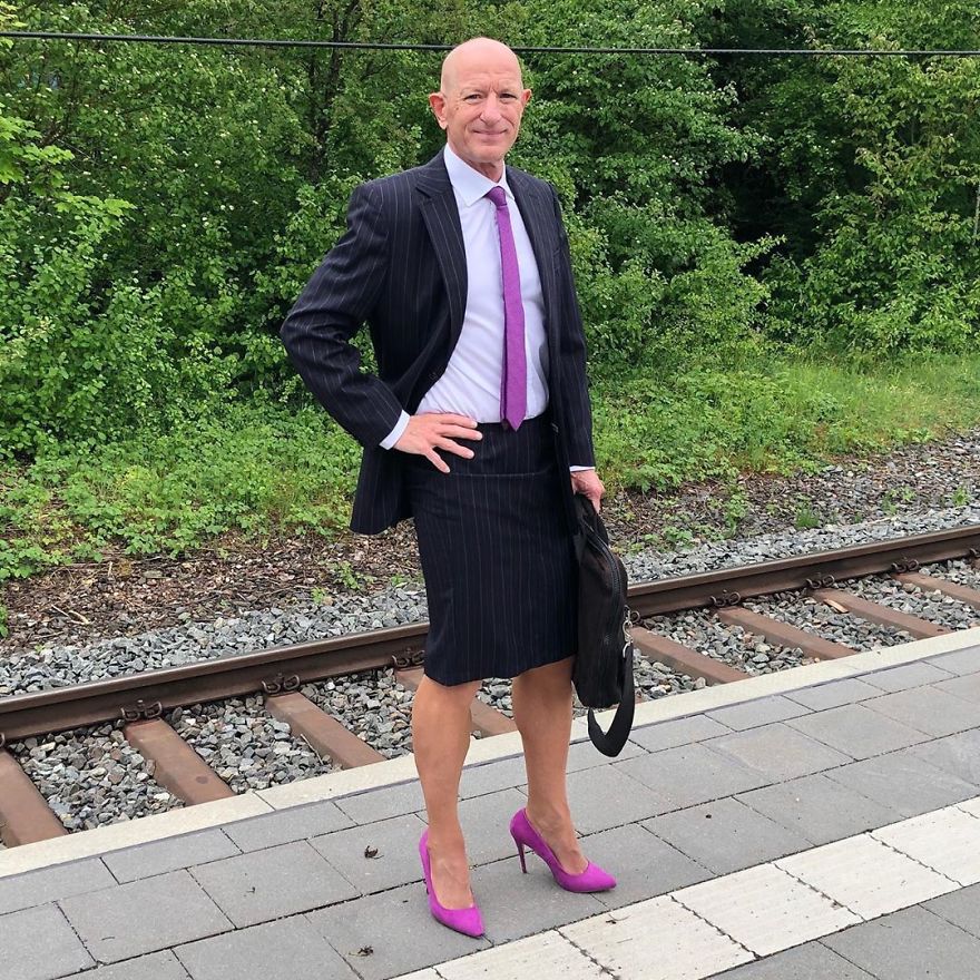 Mark Bryan in a black with white stripes skirt suit, white shirt and a purple tie and high heels
