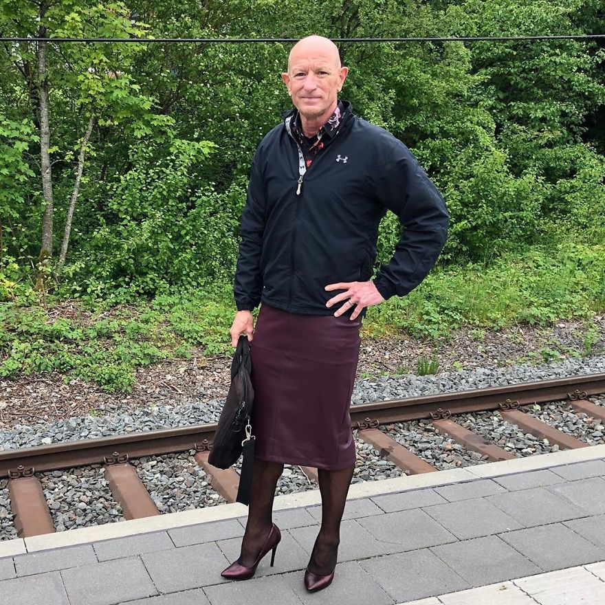 Mark Bryan standing near the railway and wearing a black jacket, bordo skirt, and glossy high heels