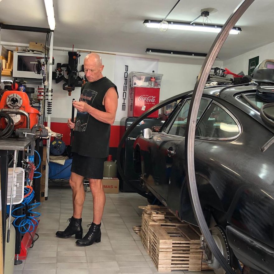 Mark Bryan in a sleeveless black shirt, skirt and leather high heel boots is standing in a garage