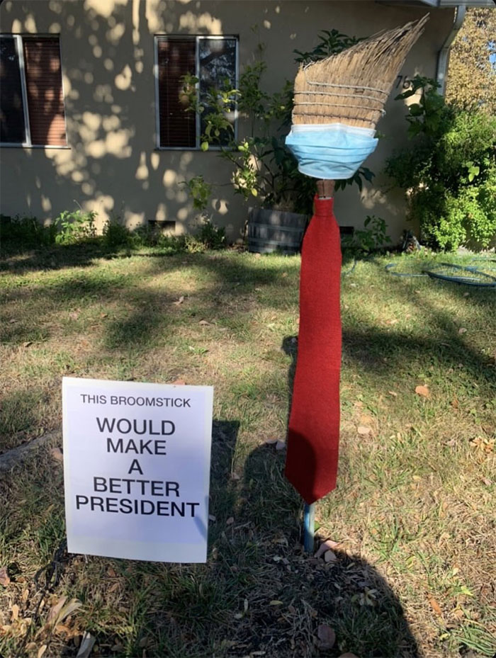 Halloween decoration of a broomstick wearing a face mask and red tie with a sign that reads it would make a better president.