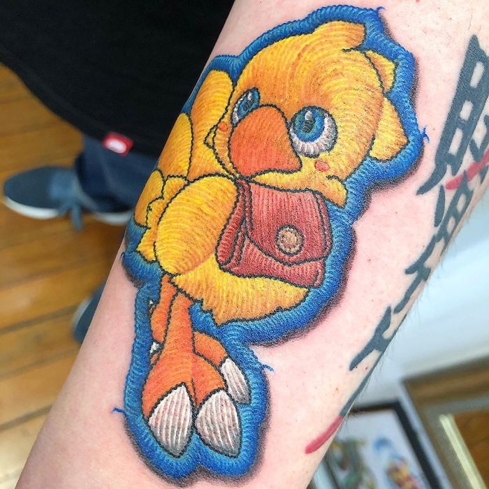 Tattoo of a yellow bird resembling a sewn-on patch on a person's arm.