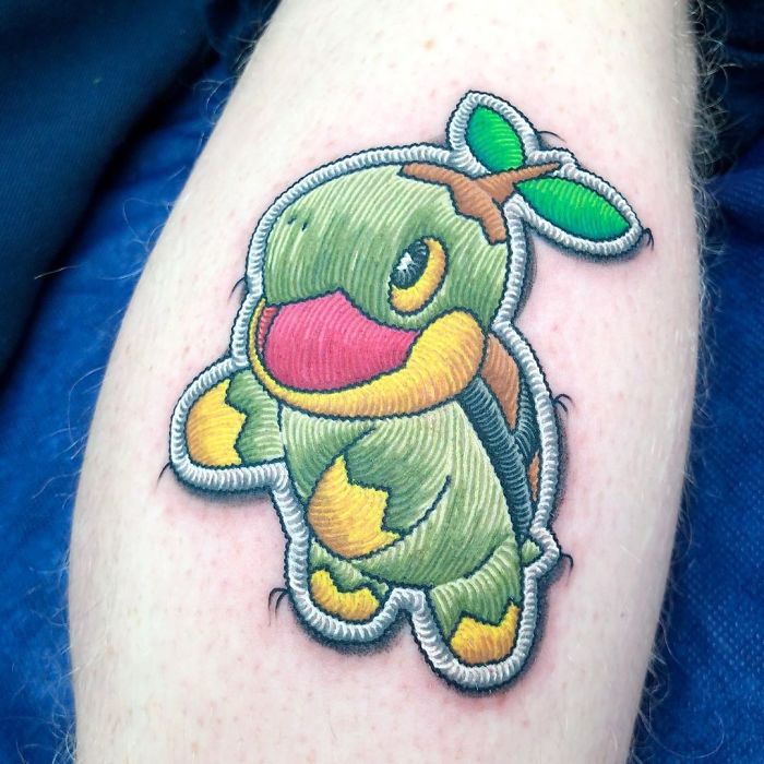 Tattoo resembling a sewn-on patch of a cartoon dinosaur on skin, showcasing impressive artistic detail.