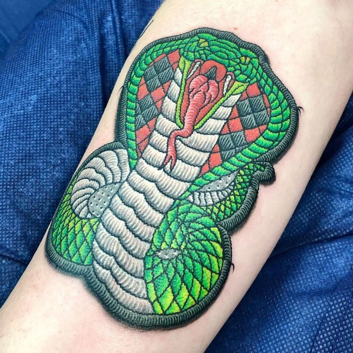 Tattoo resembling a sewn-on patch of a vibrant green cobra on forearm, showcasing impressive stitching detail.