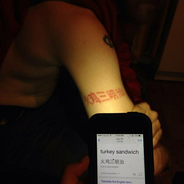 Person with a tattoo in a foreign language, humorously translated as "turkey sandwich" on a phone screen.