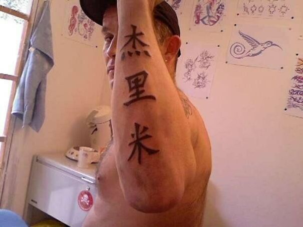 Man with foreign language tattoo, displaying characters on his forearm in a tattoo parlor.