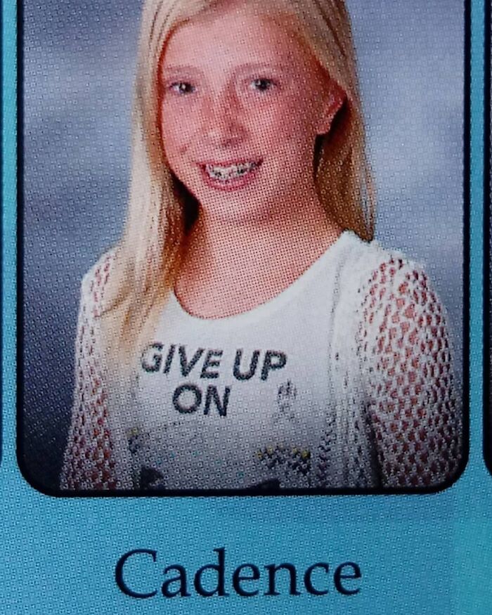 Blonde girl in school photo with a humorous expression, wearing a T-shirt that says, "Give Up On."