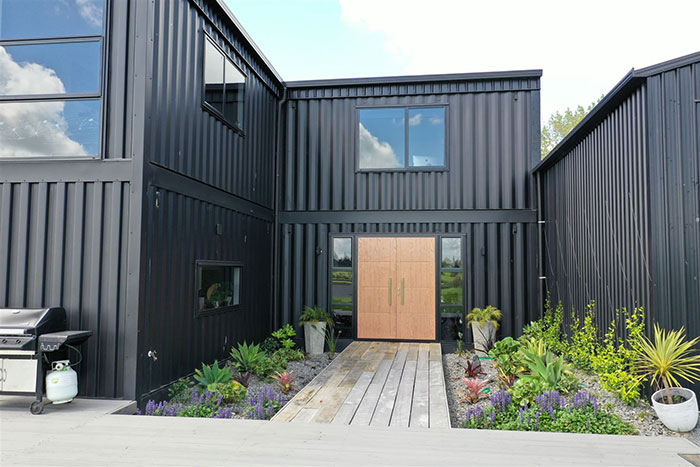 Modern house made from shipping containers with stylish exterior, featuring wooden doors and colorful landscaping.