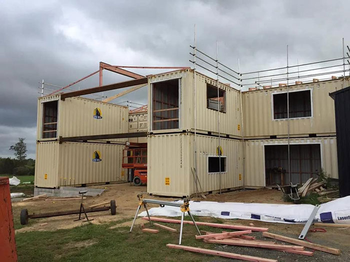 Shipping container house under construction, showcasing innovative use of 12 containers with visible scaffolding.