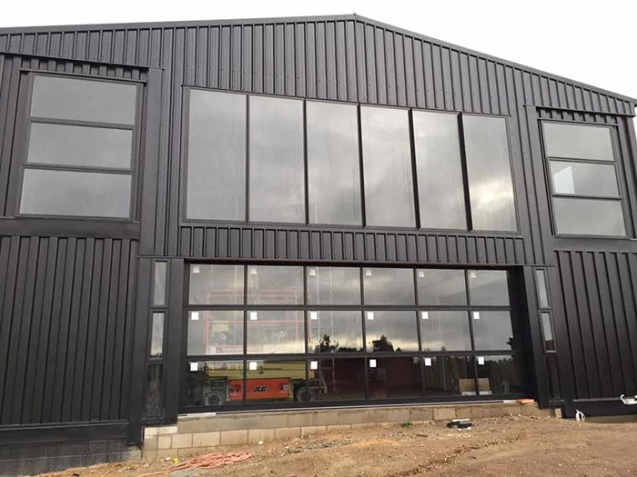Modern house exterior built from 12 shipping containers with large windows and sleek black facade.