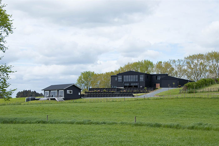 House built from shipping containers with modern black exterior, set in a lush green landscape.