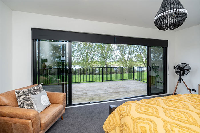 Interior of house built with shipping containers, featuring a cozy bedroom with a yellow bedspread and large glass doors to a deck.