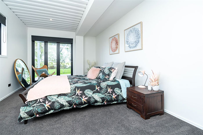 Interior of a shipping container house with a stylish bedroom, featuring floral bedding and modern decor.