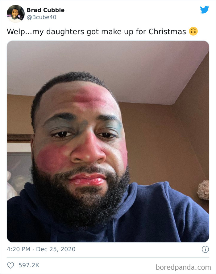 Man with colorful makeup on his face after a visit to his daughters' beauty salons, wearing a navy blue hoodie indoors.