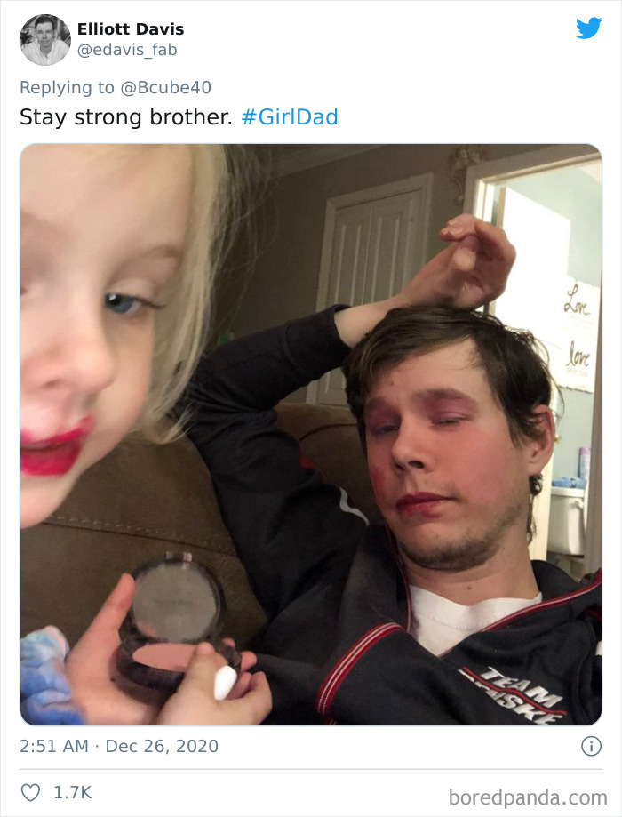 Man with makeup on face looking tired after visit to daughter's beauty salon at home with child applying makeup.