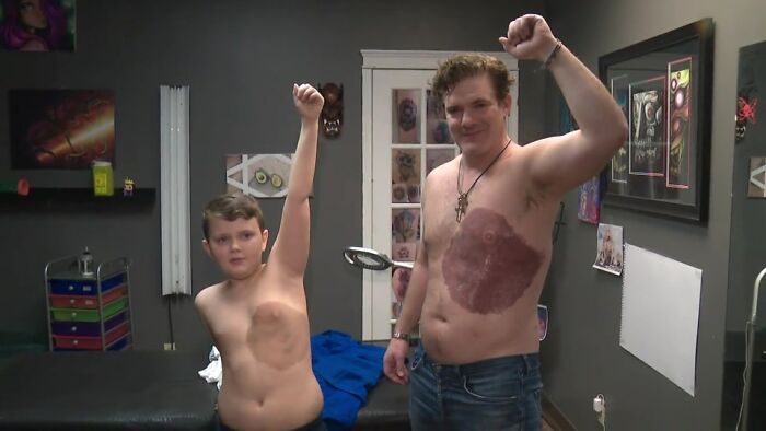 Dad with identical tattoo to match son's birthmark, both raising arms in tattoo studio.