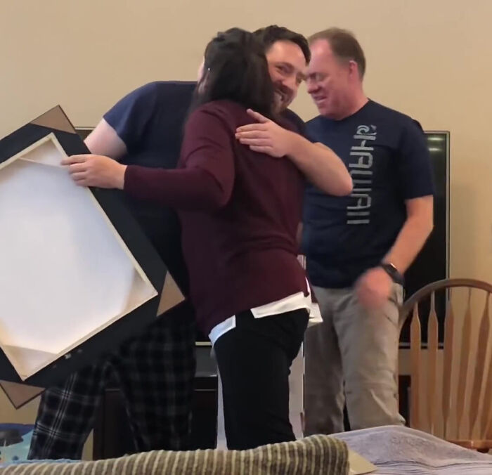 Three people smiling and hugging while holding a framed Obi-Wan Kenobi portrait.