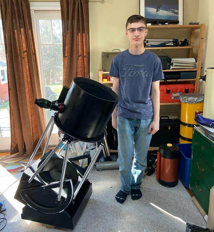 Boy standing near a big black telescope in room 