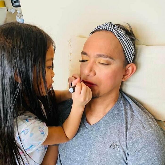 Dad with a headband getting makeup applied by his daughter at her beauty salon playtime.