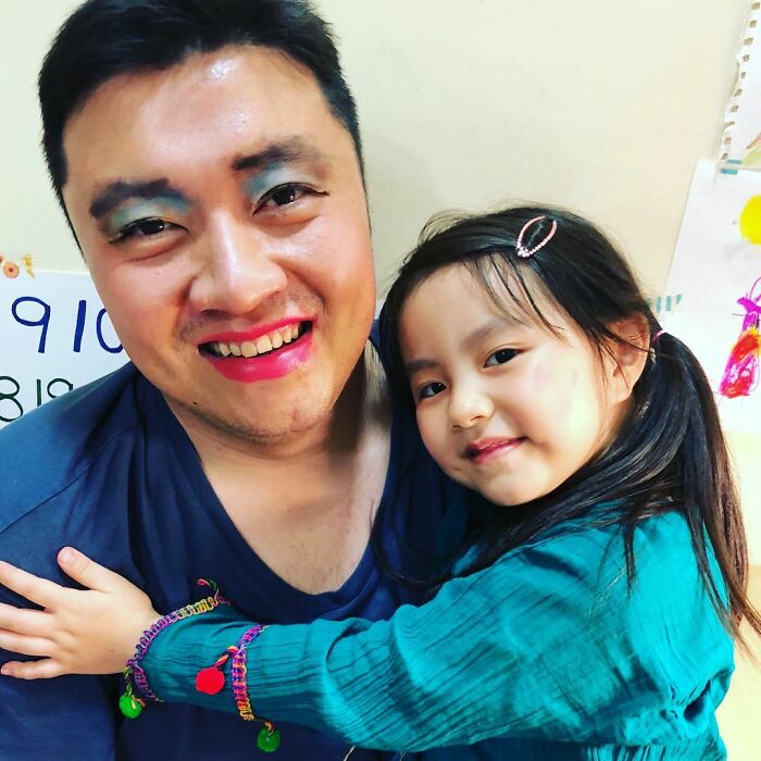 Dad with colorful makeup hugs his smiling daughter after a fun visit to their playful beauty salon session at home.
