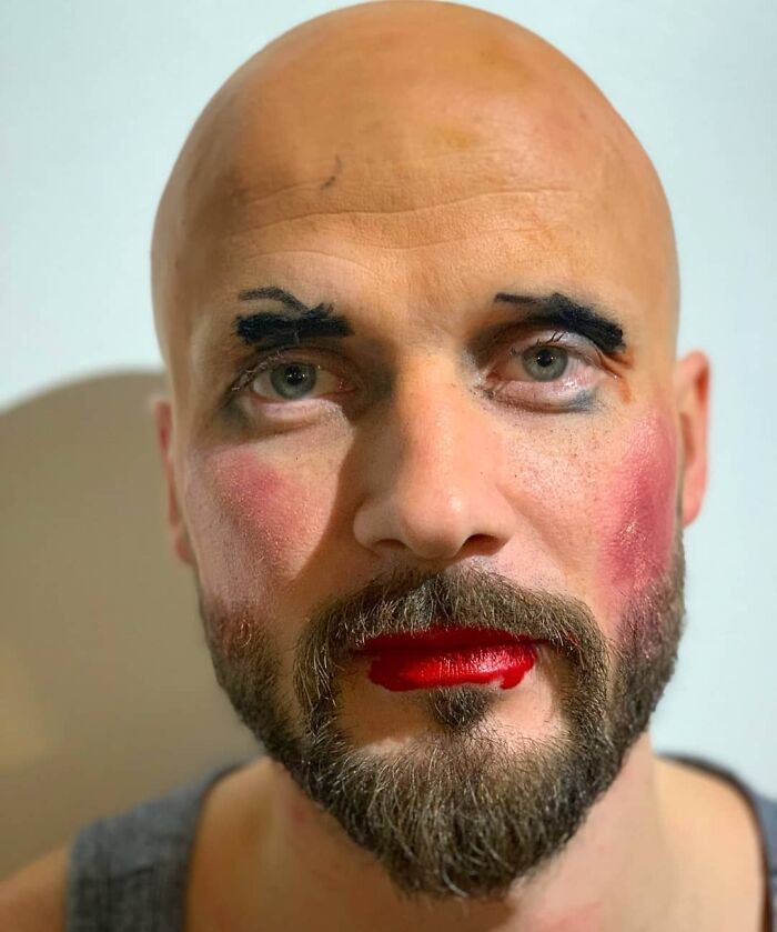 Bald man with a beard wearing exaggerated makeup, showing a humorous makeover from daughters' beauty salons visit.