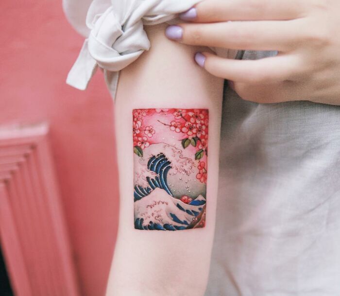 Beautiful body art tattoo featuring waves and cherry blossoms on an arm.