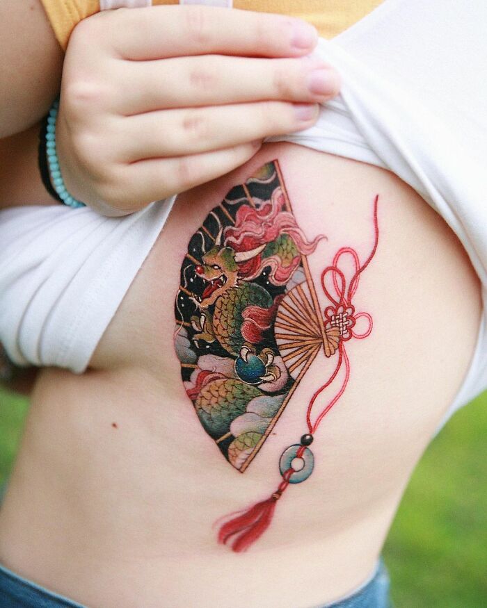 Beautiful body art with a colorful dragon and fan tattoo design on a person's side.