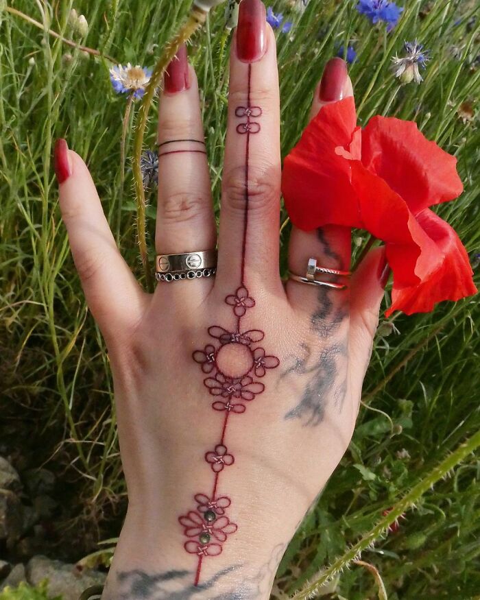 Beautiful body art by tattoo artist, displaying intricate floral design on a hand with a red flower.