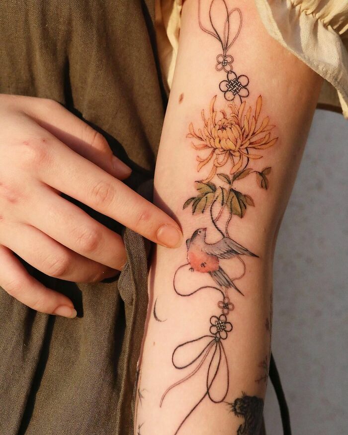 Intricate body art by tattoo artist featuring a flower and bird design on the forearm.