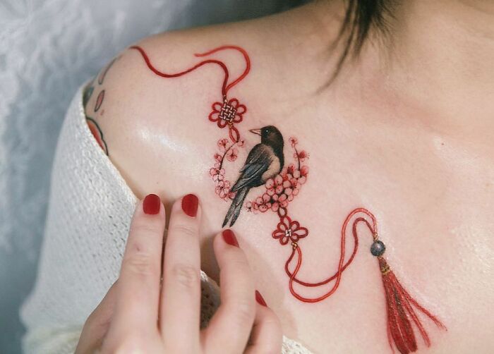 Beautiful body art by tattoo artist featuring a bird and floral design on a person's shoulder with red accents.