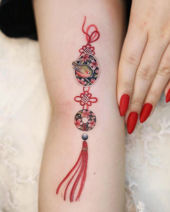 Beautiful body art by tattoo artist featuring intricate red and floral design on forearm.