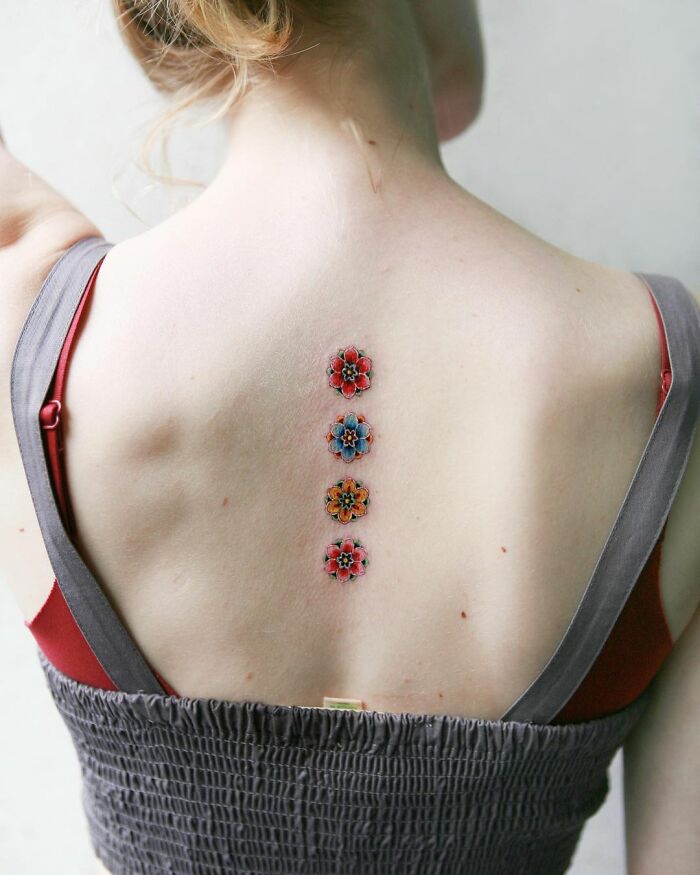 Back with colorful floral body art tattoo by Sion Kwak, featuring intricate designs along the spine.