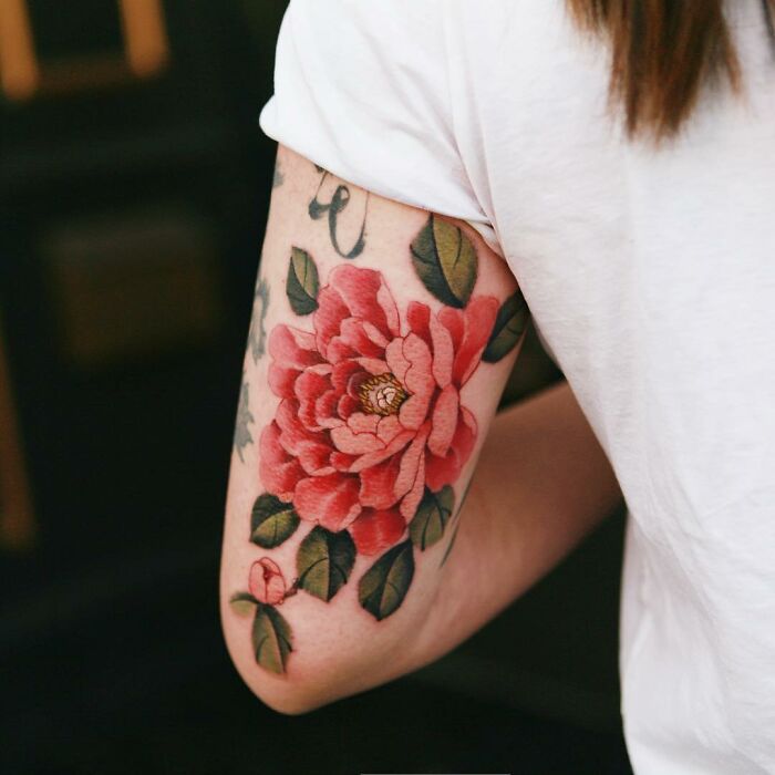 Beautiful body art with a detailed red flower tattoo by artist Sion Kwak on a person's arm.
