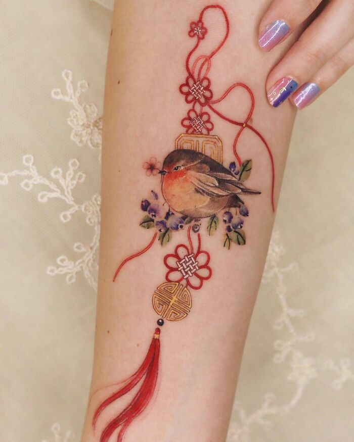Beautiful body art featuring a bird and decorative elements by tattoo artist Sion Kwak on an arm.