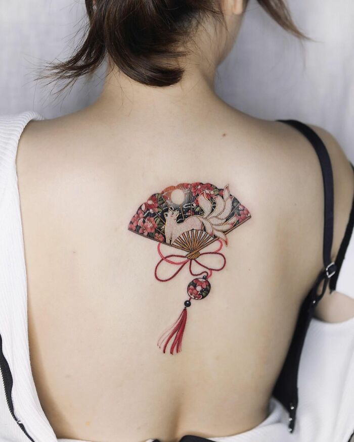 Back tattoo by Sion Kwak featuring intricate design with a fan, fox, and floral elements.