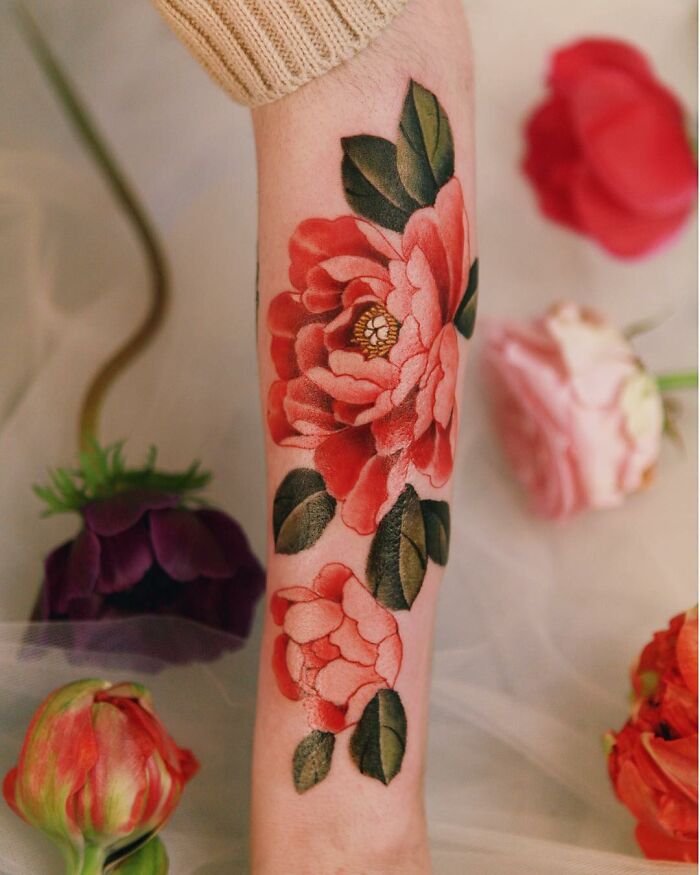 Beautiful body art featuring vibrant floral tattoos on a forearm, surrounded by fresh flowers.