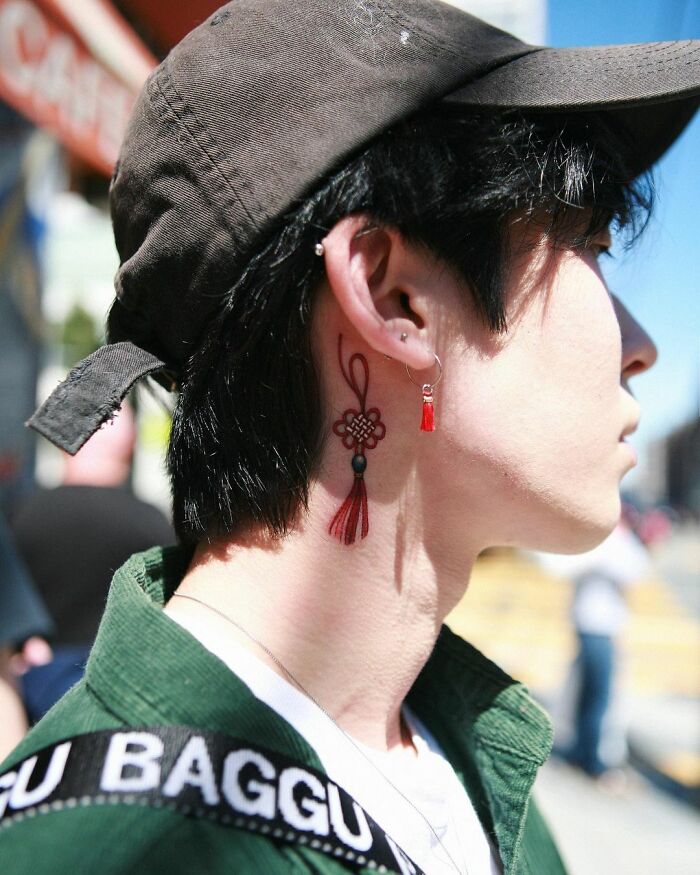 Tattoo artist Sion Kwak's intricate red tassel neck tattoo on a person in a cap, showcasing beautiful body art.