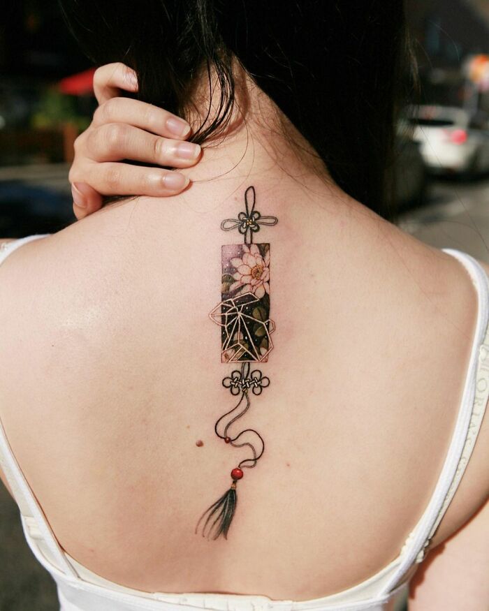 Beautiful body art by tattoo artist on woman's upper back, featuring floral and geometric design elements.