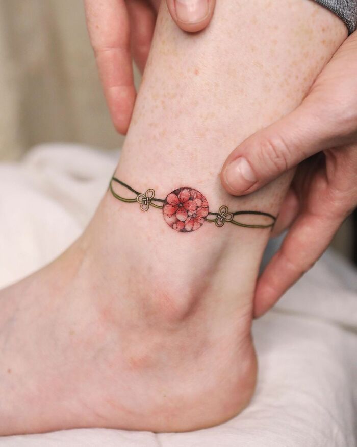 Delicate floral ankle tattoo by artist Sion Kwak, showcasing intricate body art.
