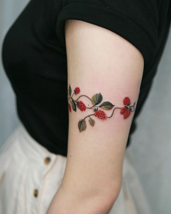 Floral body art tattoo featuring berries and leaves on an arm, showcasing Sion Kwak's intricate design.