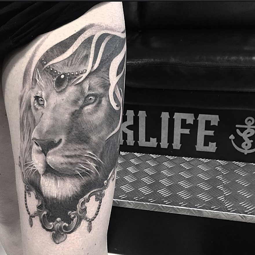Black and gray realism tattoo of a lion by Swedish artist on a person's arm, in front of a seat with "KLIFE" text.