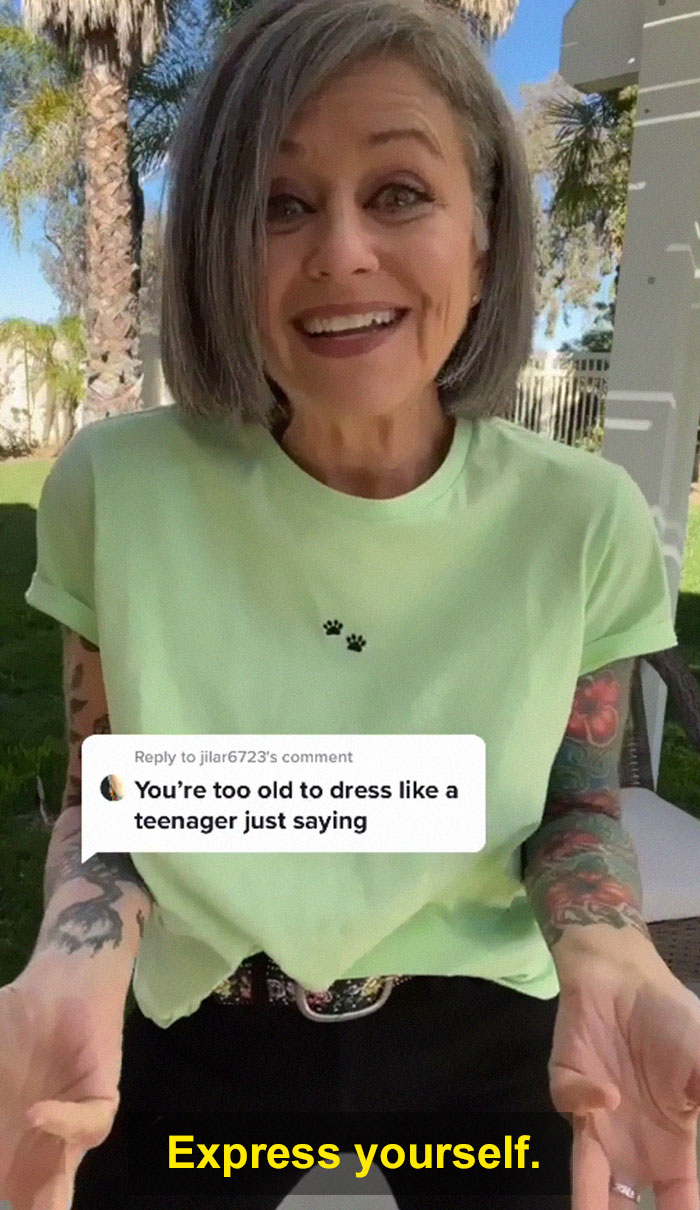 Woman in her 50s smiling outdoors wearing a green tee with tattoos, showing confidence despite age dress criticism.