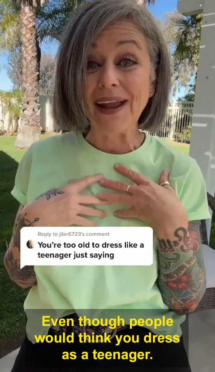 Woman in her 50s with tattoos responds confidently about dressing like a teenager in a casual green shirt outdoors.