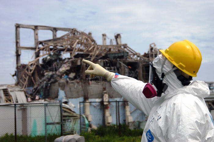 Person in protective gear and yellow helmet pointing at damaged building, illustrating interesting facts people didn’t learn at school.