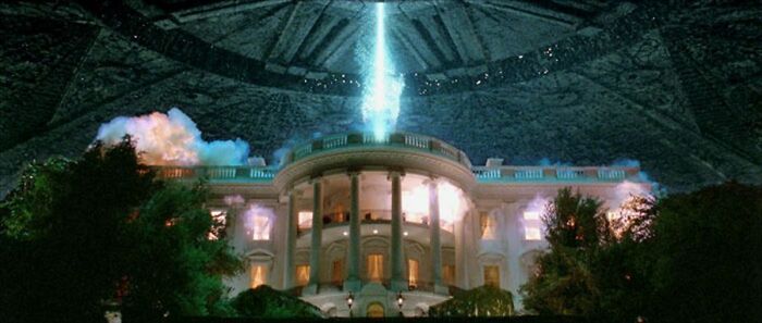 The White House illuminated by a bright beam of light inside a large domed alien spaceship in a sci-fi scene.