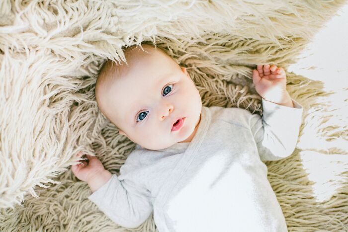 Baby with blue eyes lying on a soft textured rug, illustrating curiosity and discovery in today I learned facts.