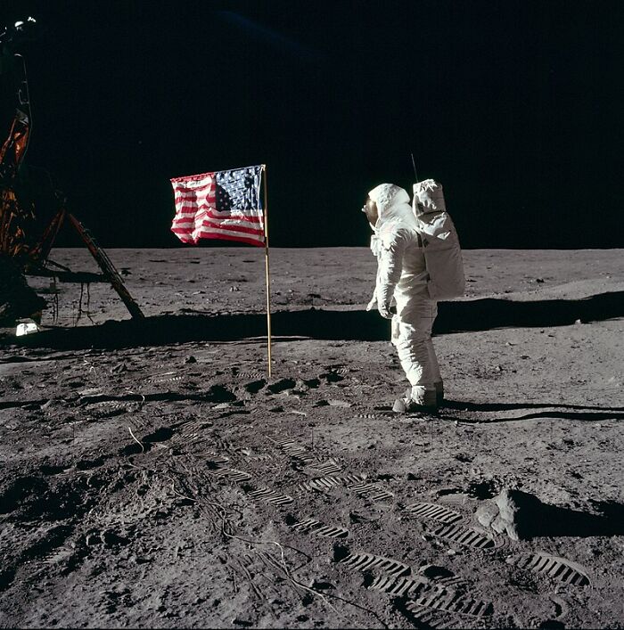 Astronaut standing next to American flag on the moon surface illustrating interesting facts people didn’t learn at school.