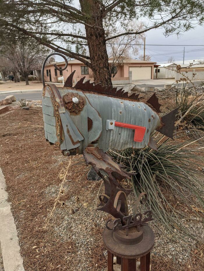 Creative and cool mailbox shaped like a fish made from metal with a red flag in a residential yard.