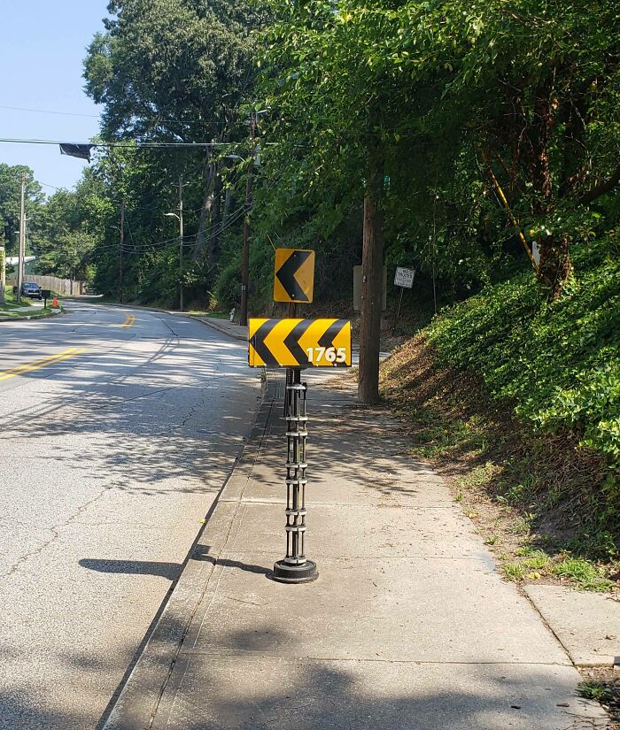 Creative mailbox designed to resemble a road sign with yellow and black chevrons, blending into the roadside environment.
